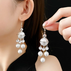 Detail of long tassel earrings featuring large white pearl and silver planet ring with zircons