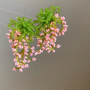 Detailed view of handmade beaded earrings with green flower top and pink fringe tassels
