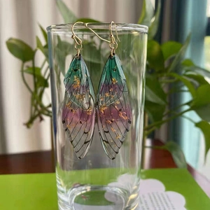 Detailed macro of cicada wing earrings with green-purple gradient and gold foil accents