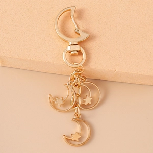 Detailed close-up of a gold metal keychain with hollow moon and star charms on a beige base