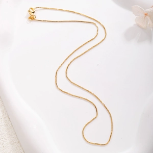 Detail of gold-plated box chain necklace with lobster clasp on white decorative tray