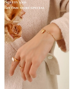 Close-up of gold heart pendant bracelet and gemstone rings on soft knit background