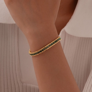 Detail of gold woven chain bracelet featuring sparkling green round cubic zirconia stones