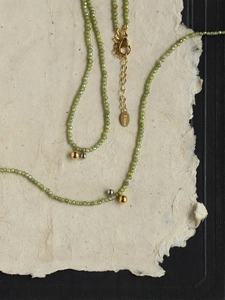Detailed shot of olive green beaded necklace with gold and silver accents and S.Steel tag