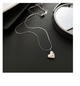 Close-up of heart pendant necklace with polished silver finish on a minimalist surface