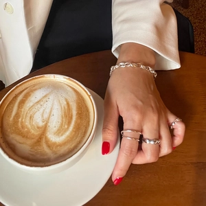 Minimalist 925 sterling silver rings and chain bracelet on hand with coffee cup