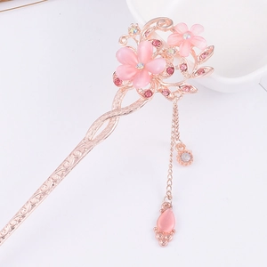 Macro detail of rose gold hair pin featuring pink cat eye flowers and sparkling tassels