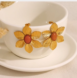Detail of vintage gold flower earrings with red stone on a white ceramic cup