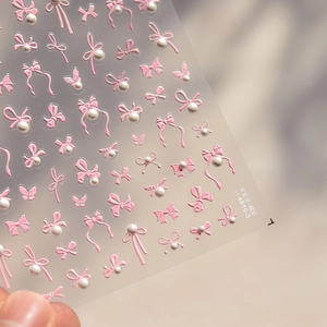 Macro detail of 3D embossed nail stickers featuring pink ribbons and white pearls