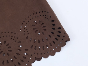 Detailed close-up of dark brown suede-like fabric with laser-cut floral hem patterns