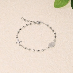 Close-up of silver beaded bracelet with religious cross and Mary medallion on beige texture