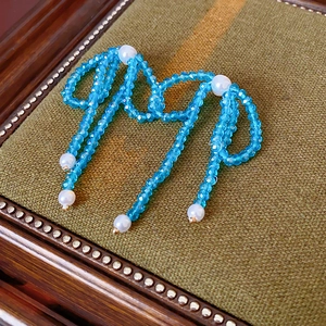 Detail of bow-shaped stud earring with blue faceted beads and white faux pearls