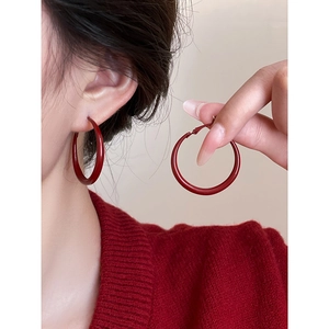 Close-up of red oversized hoop earrings featuring a smooth matte finish on a model