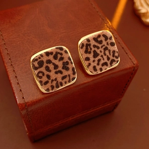 Détail de boucles d'oreilles carrées léopard avec bord doré sur une boîte en cuir brun
