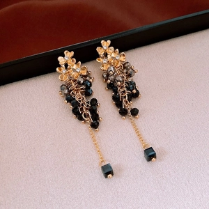 Macro detail of golden flower earrings with black crystal tassels and square pendants