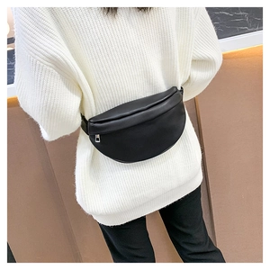 Detailed view of a black faux leather chest bag worn over a white chunky knit sweater