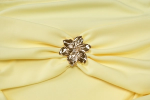 Detalle de una hebilla de metal dorado con forma de flor en tela plisada amarilla