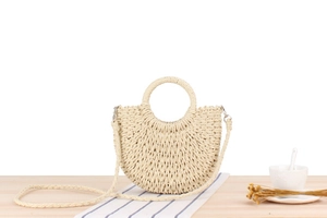 Detail of semi-circular woven straw bag with ring handle and strap on wooden surface