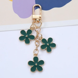 Close-up of golden keychain with three dark green flower charms on beige background
