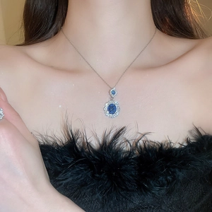 Close-up of a blue oval gemstone necklace with diamond halo on a model neck