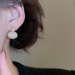 Close-up of elegant gold-plated stud earrings with pavé zircons worn on a model ear