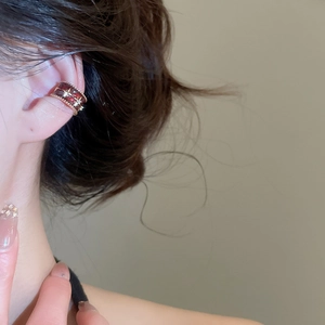 Close-up of zircon bow ear cuff with deep red glaze and gold star accents on model