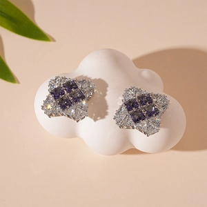 Macro view of geometric stud earrings featuring purple cubic zirconia on a white cloud prop