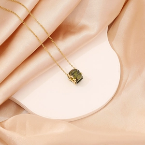 Minimalist gold necklace featuring a square green gemstone pendant on a silk background