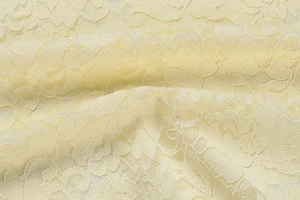 Detailed macro shot of pale yellow floral lace fabric with intricate embroidery and mesh