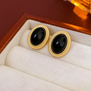 Close-up of vintage gold-rimmed oval black earrings on a soft beige velvet jewelry display