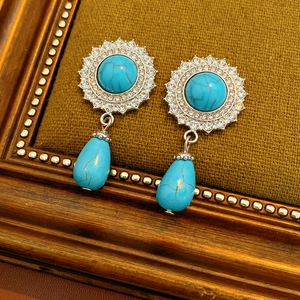 Macro view of vintage silver drop earrings with turquoise stones on green textured fabric