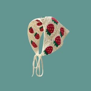 Detail of handcrafted crochet headscarf featuring vibrant red strawberry embroidery patterns