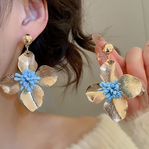 Detailed close-up of gold flower earrings with blue stamen on a female model