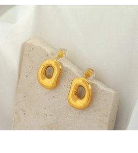 Close-up of golden irregular oval earrings on stone with soft lighting and 18k finish