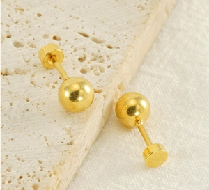 Detail of gold bead earrings with mirror finish on textured beige stone surface
