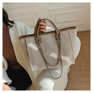 Detail of beige woven tote bag with brown leather trim and metal chain strap