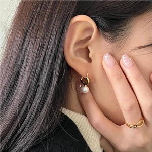 Detail of golden heart earrings with pearl drops worn by a model in natural lighting