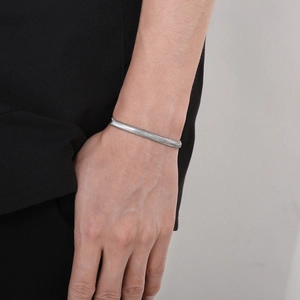 Close-up of a minimalist silver flat snake chain bracelet on a wrist against black clothing