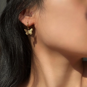 Close-up of 18K gold plated butterfly drop earrings on model with detailed textures