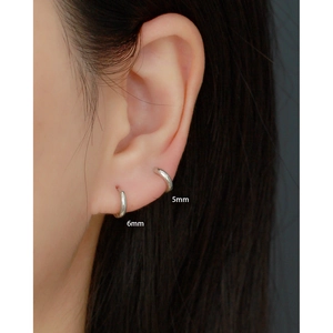 Close-up of minimalist silver huggie earrings in 5mm and 6mm sizes on ear