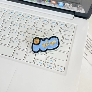 Close-up of a blue plush embroidery pin with a smiley face on a white keyboard