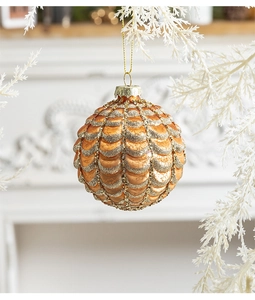 Golden Christmas bauble with fish-scale glitter texture hanging on a snowy winter branch