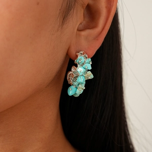 Close-up of irregular turquoise stones on a silver textured C-shaped earring