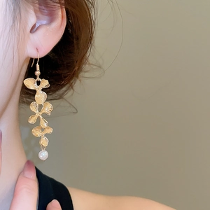 Detail of long gold flower earrings with white pearl tassel hanging from a female model
