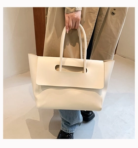 Close-up of cream white leather tote bag being held by a model in a minimalist setting
