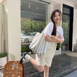 Lifestyle shot of large canvas tote bag with cream vertical stripes and casual chic outfit