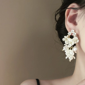 Detail shot of multi-layered white floral earrings with golden beads on female model