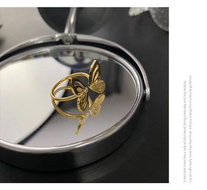 Macro shot of an adjustable hollow butterfly ring with polished gold finish on a mirror