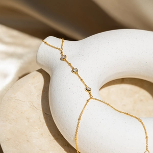Dettaglio del bracciale a catena dorata con tre zirconi chiari su un vaso di ceramica
