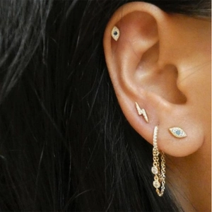 Detail shot of gold S925 earrings featuring evil eye and lightning studs with rhinestones